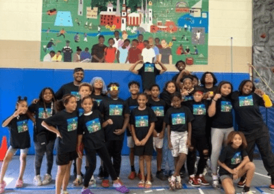 Young kids gathered in front of the mural wearing shirts of the mural